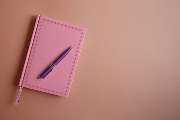 Purple metal pen on a pink notebook or diary, on a pink paper background flat lay