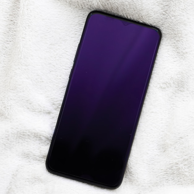 Purple mobile device on white blanket in winter smartphone flatlay mockup as app template and brand ...