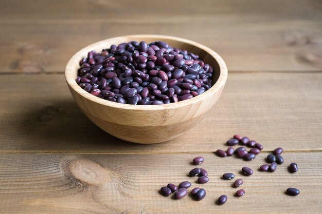 Purple raw beans in bowl close up on wooden background.