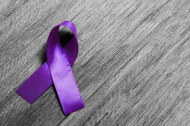 Nastro viola come simbolo della giornata mondiale contro il cancro su struttura in legno bianco e nero