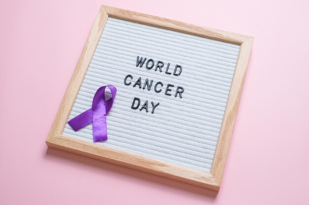 Purple ribbon as symbol of World Cancer Day over pink color background