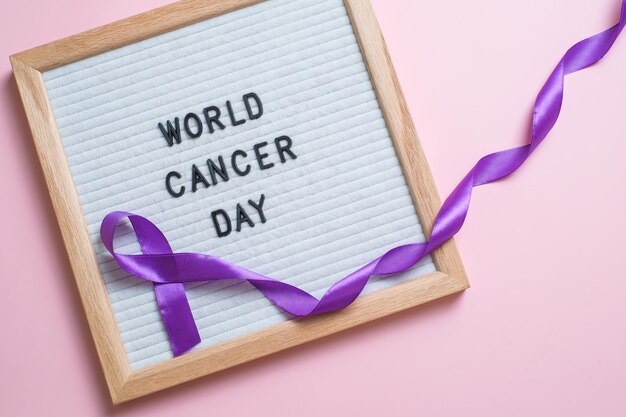 Purple ribbon as symbol of World Cancer Day over pink color background