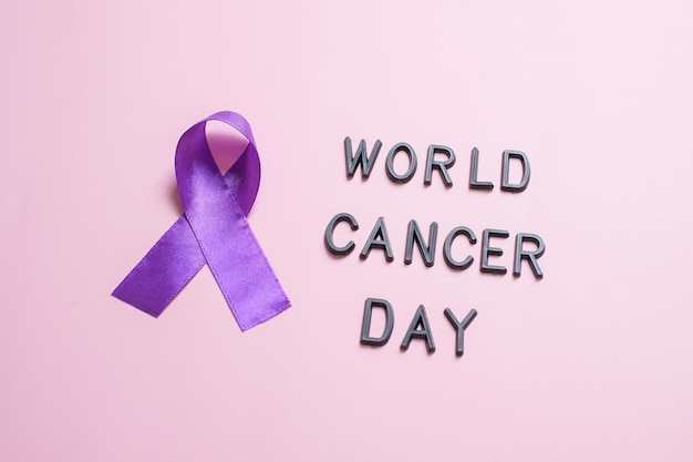 Purple ribbon as symbol of World Cancer Day over pink color background