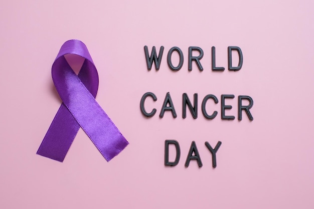 Purple ribbon as symbol of world cancer day over pink color\
background