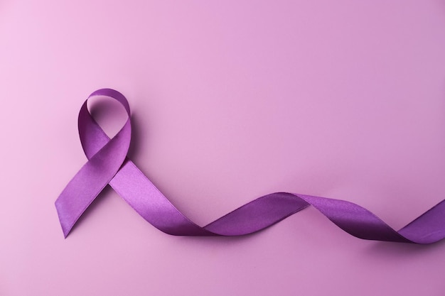 Фиолетовая лента как символ Всемирного дня борьбы против рака на фиолетовом фоне копией пространства