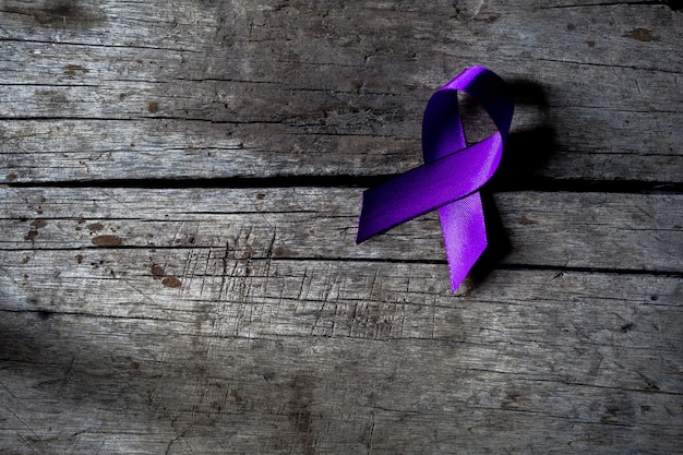 A purple ribbon on a dark gray rustic wooden surface, violence against women concept