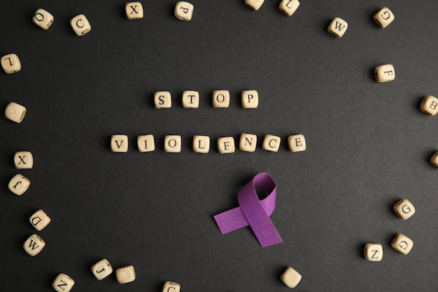 Purple ribbon and phrase STOP VIOLENCE made of wooden cubes on black background flat lay