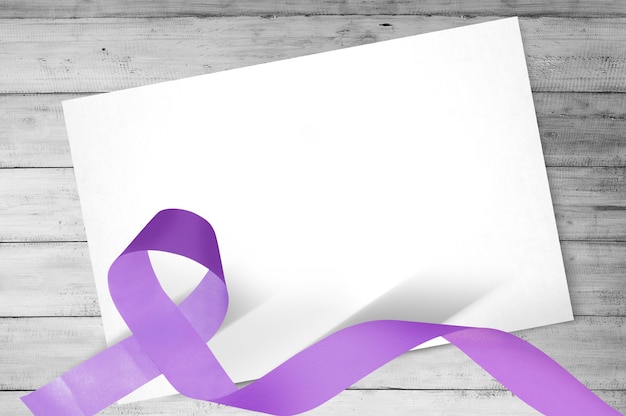 Purple ribbons with blank white paper on wooden background.\
world cancer day concept. blank white paper for copy space