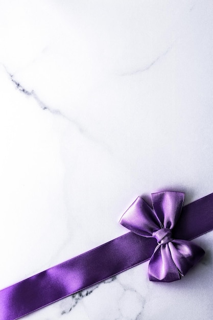 Purple silk ribbon and bow on luxury marble background holiday flatlay backdrop