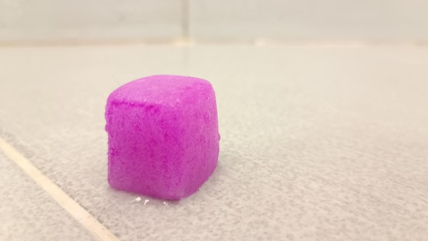 A purple square of soap sits in a bathtub with a white background.