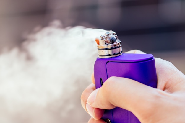 Photo purple vape in a man's hand on a modern background.