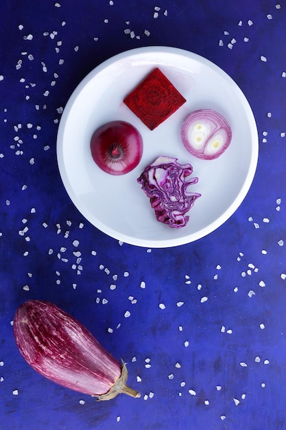 白いプレートに紫の野菜 海塩の結晶と青の背景に野菜の組成 上からのクローズ アップ ビュー