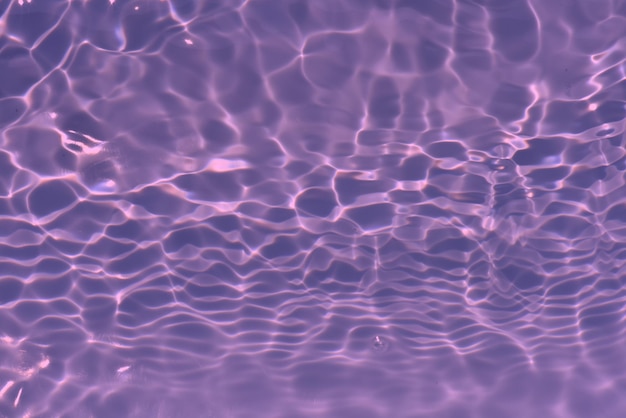 Purple water background that has ripples and the sun reflecting on it