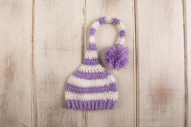 Photo purple and white striped hat with a pom pom on a wooden background.