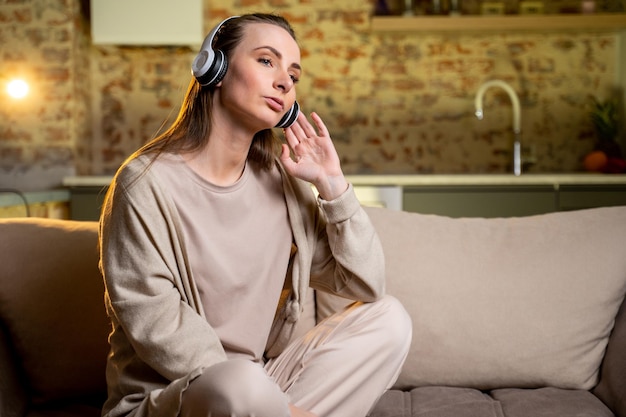 Purposeful young woman listening to music with headphones dancing while sitting at home on the couch