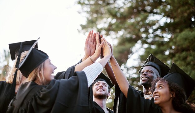 Photo pursuing a bright future shot of a group of students giving each other a high five on graduation day