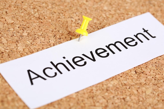 Push pin on paper with word achievement on cork board