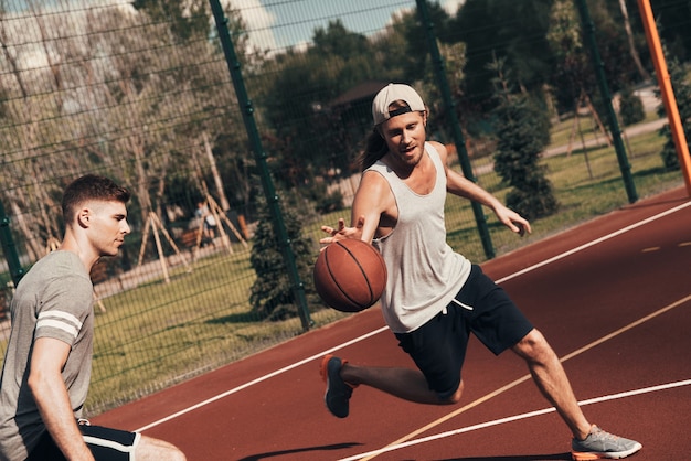 Pushing hard. Two young men in sports clothing playing basketball while spending time outdoors