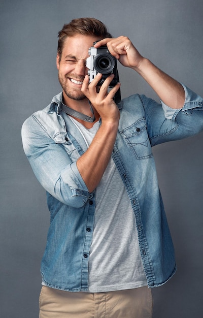 Put your happy face on Portrait of a happy young man holding up a camera while posing against a gray background in the studio