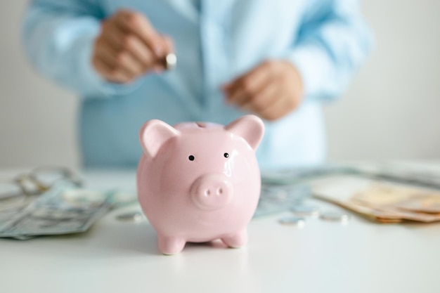 Putting a coin into a piggy bank close-up. woman hand holding money bank note dollar with piggy for saving money wealth and finance