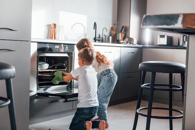 Putting food into oven Little boy and girl preparing Christmas cookies on the kitchen