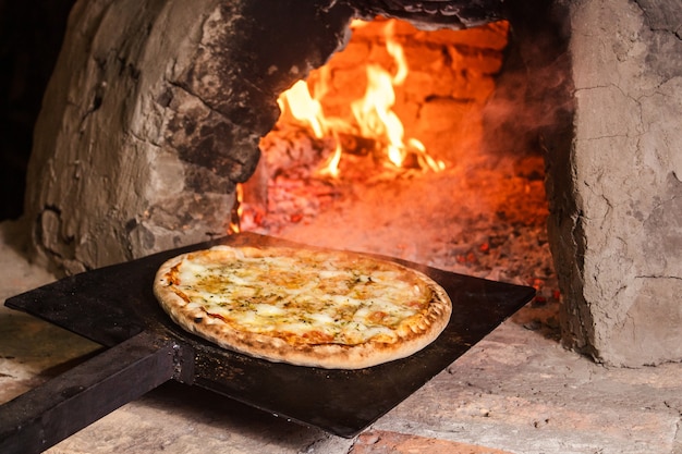 Photo putting a four-cheese pizza in a paraguayan handmade oven (tatakua).