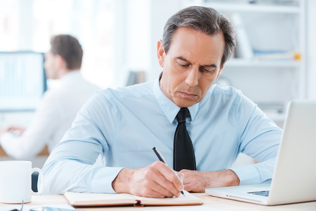 Putting his ideas on paper. Serious businessman in formalwear writing in note pad 