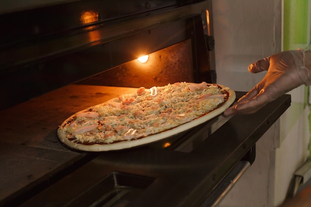 Putting seafood pizza into oven Preparing Italian traditional pizza into pizzeria.