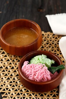 米粉​スト​ランド​で​作られた​プトゥマヤン​または​ペチュロインドネシア​の​伝統的​な​ジャワ​の​スナック​は​、​ココナッツ​ミルク​と​パームシュガーシロップ​を​添えた​食品​着色料​で​ボール​に​丸められました