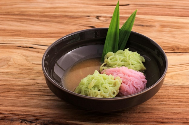 Putu Mayang or Petulo Indonesian Traditional Javanese Snack Made of Rice Flour Strands Curled up into a Ball with Food Coloring Served with Coconut Milk and Palm Sugar Syrup on the Table