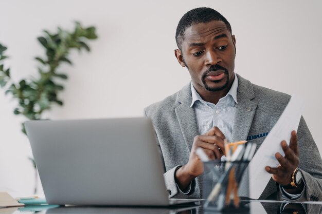 Puzzled african american businessman discussing working project online by video call at laptop