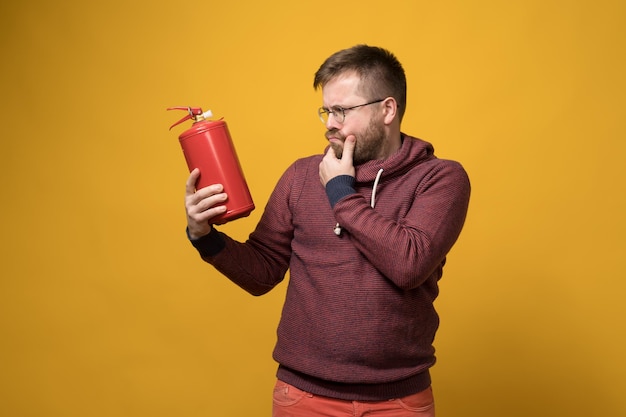 Puzzled man with glasses holds a fire extinguisher in hand and\
looks at it thoughtfully