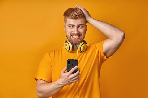 Puzzled man with red beard forgets about something holds mobile phone