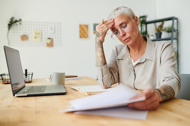 オフィスで事務処理をしながら額をこすりながら丸い眼鏡で困惑した中年の実業家