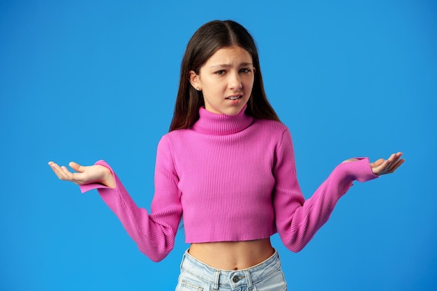 Puzzled teen girl dont know what to do on blue background in studio