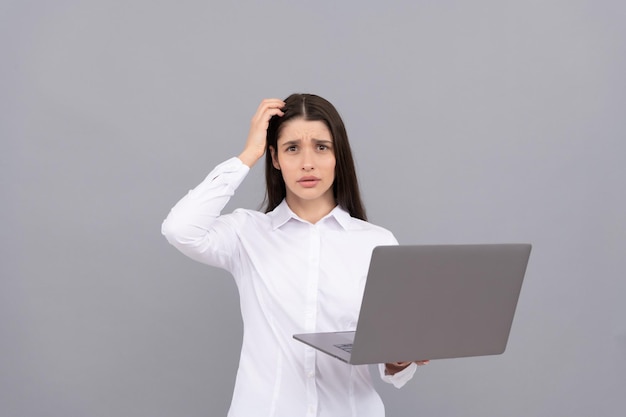 Озадаченная женщина в белой рубашке держит компьютер, у нее много проблем с работой