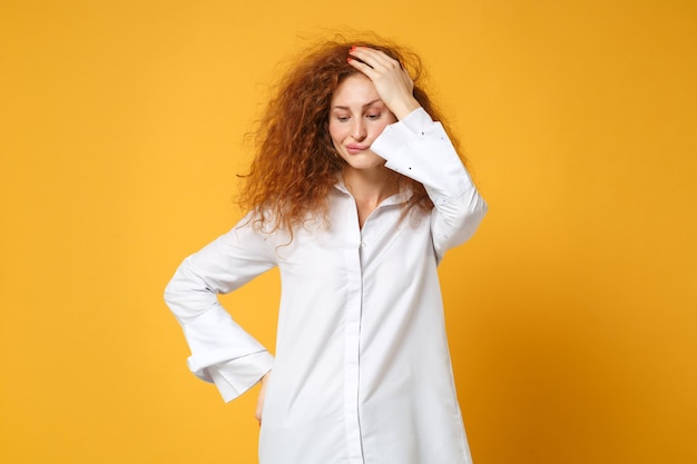Puzzled young redhead woman girl in casual white shirt posing isolated on yellow orange wall