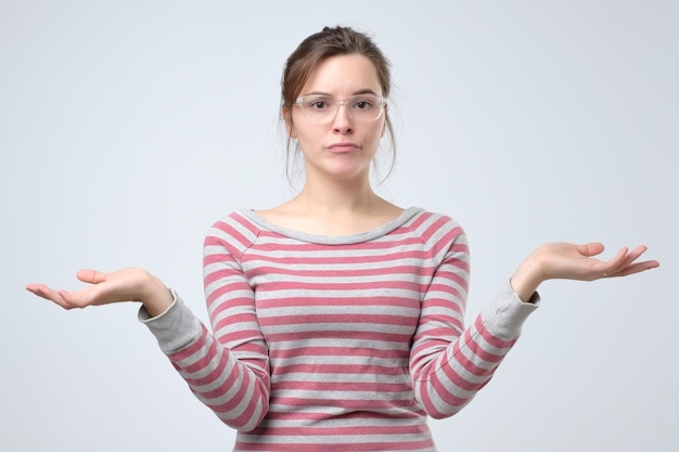 Puzzled young woman dressed casually shrugs shoulders as does not know answer