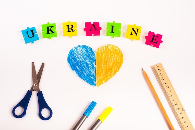 Photo puzzles of letters ukraine on a white background and paper heart painted in the color of the flag of ukraine