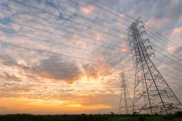 Pyloon en hoogspanningsleidingen die tegen zonsondergang zijn ontsproten