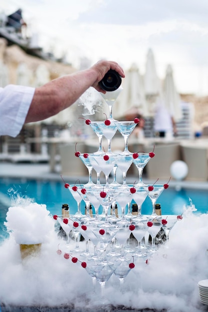 Piramide di bicchieri di champagne e ciliegie da cocktail in nuvole di fumo artificiale di ghiaccio secco