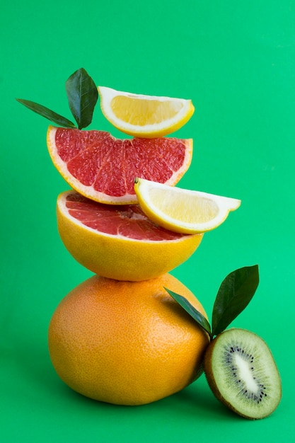 Pyramid of grapefruit, kiwi and lemon in balance  on the green background.