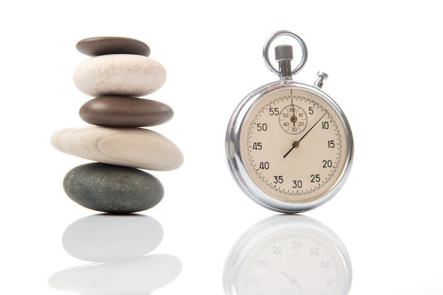 Pyramid of stones in balance and a mechanical stopwatch on a white background Time part precision Measuring the speed interval with a watch