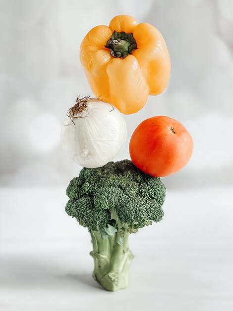 A pyramid of vegetables, broccoli, tomato, onion, pepper on a\
light background. vegetables levitation, steaming vegetables,\
healthy food concept.