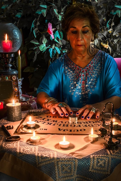 Foto pythoness-vrouwenheks of spiritualis die een seance uitvoert op een ouija-bord met veel brandende kaarsen