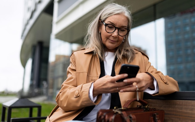 Qafqazinfo пожилая женщина с мобильным телефоном в руках на фоне здания сидит на