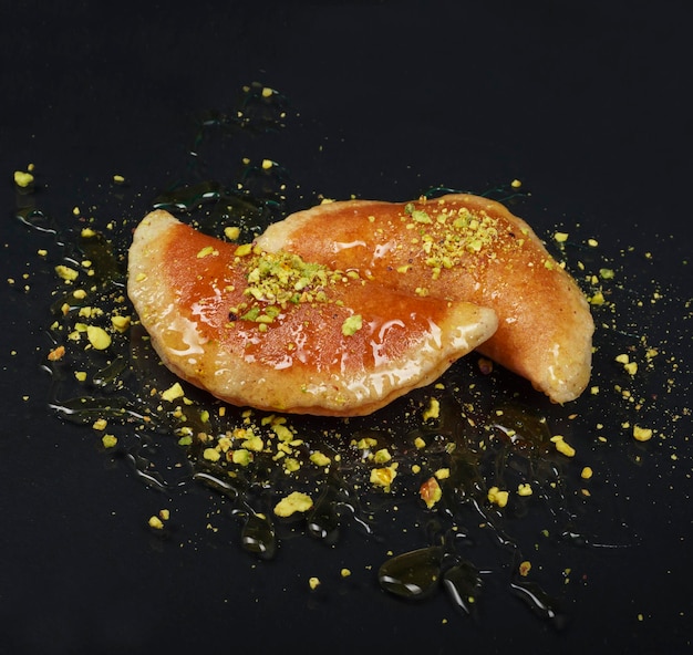 Qatayef, Traditional Arabic Ramadan Sweets with pistachio and honey on black background