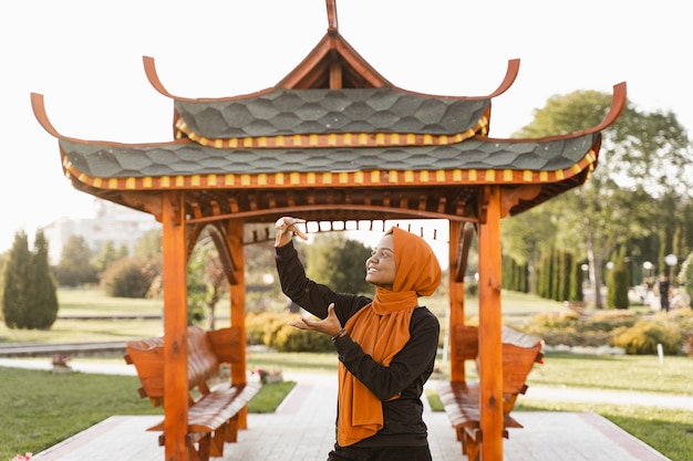 Цигун китайская медитация и спортивные тренировки на открытом воздухе. Черная мусульманка медитирует на открытом воздухе возле китайской беседки.