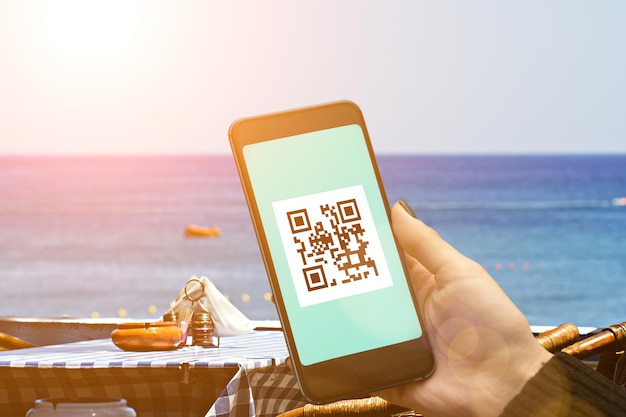 Qr-code covid19 vaccinatiecertificaat voor het bezoeken van restaurants en openbare plaatsenvaccinatiepaspoort digitale toepassing van coronavirusvaccin voor reizentoerisme hand met smartphone in zeecafé