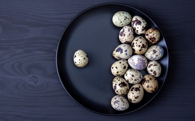 Quail eggs on black plate on wooden background. Easter holiday. Free copy space.